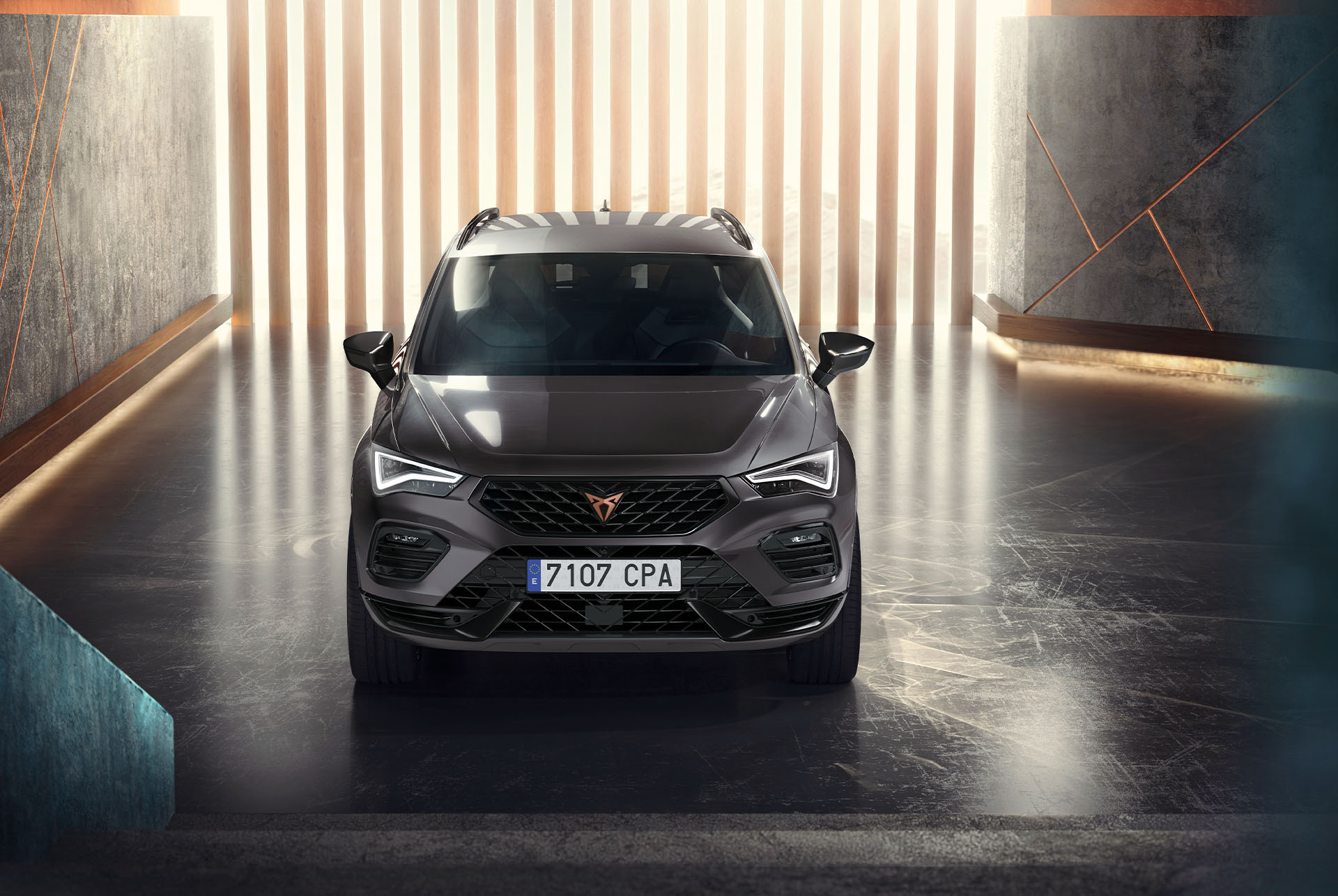 Widok z przodu szarego SUV-a Cupra Ateca w nowoczesnym, oświetlonym otoczeniu. Uwydatniony masywny przedni grill ireflektory LED. 